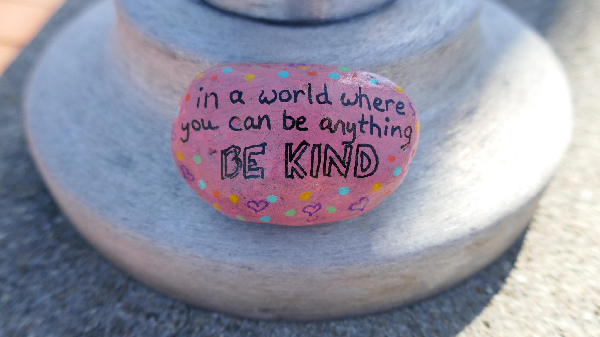 Kindness rock on pole that says "in a world where you can be anything, be kind" 