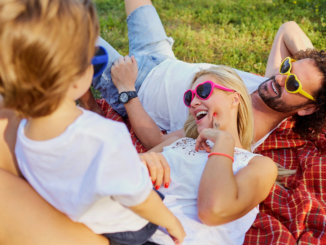 Mom and Dad laying on blanket looking up and laughing with toddler