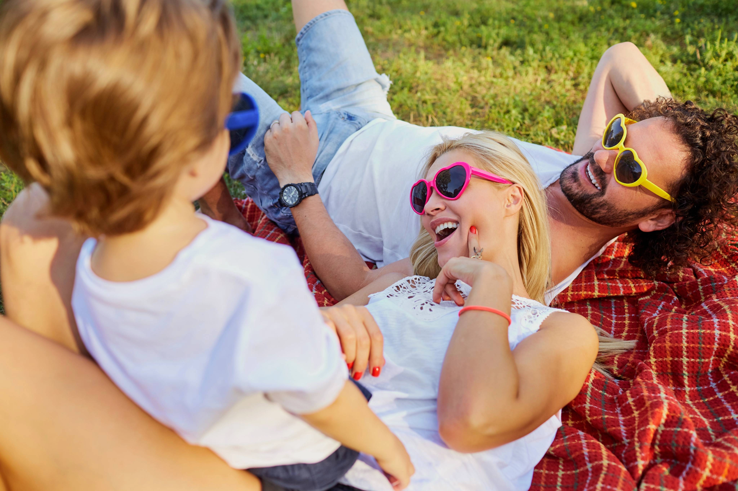 Mom and Dad laying on blanket looking up and laughing with toddler