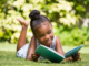 young black girl laying in the grass outside reading in the summer