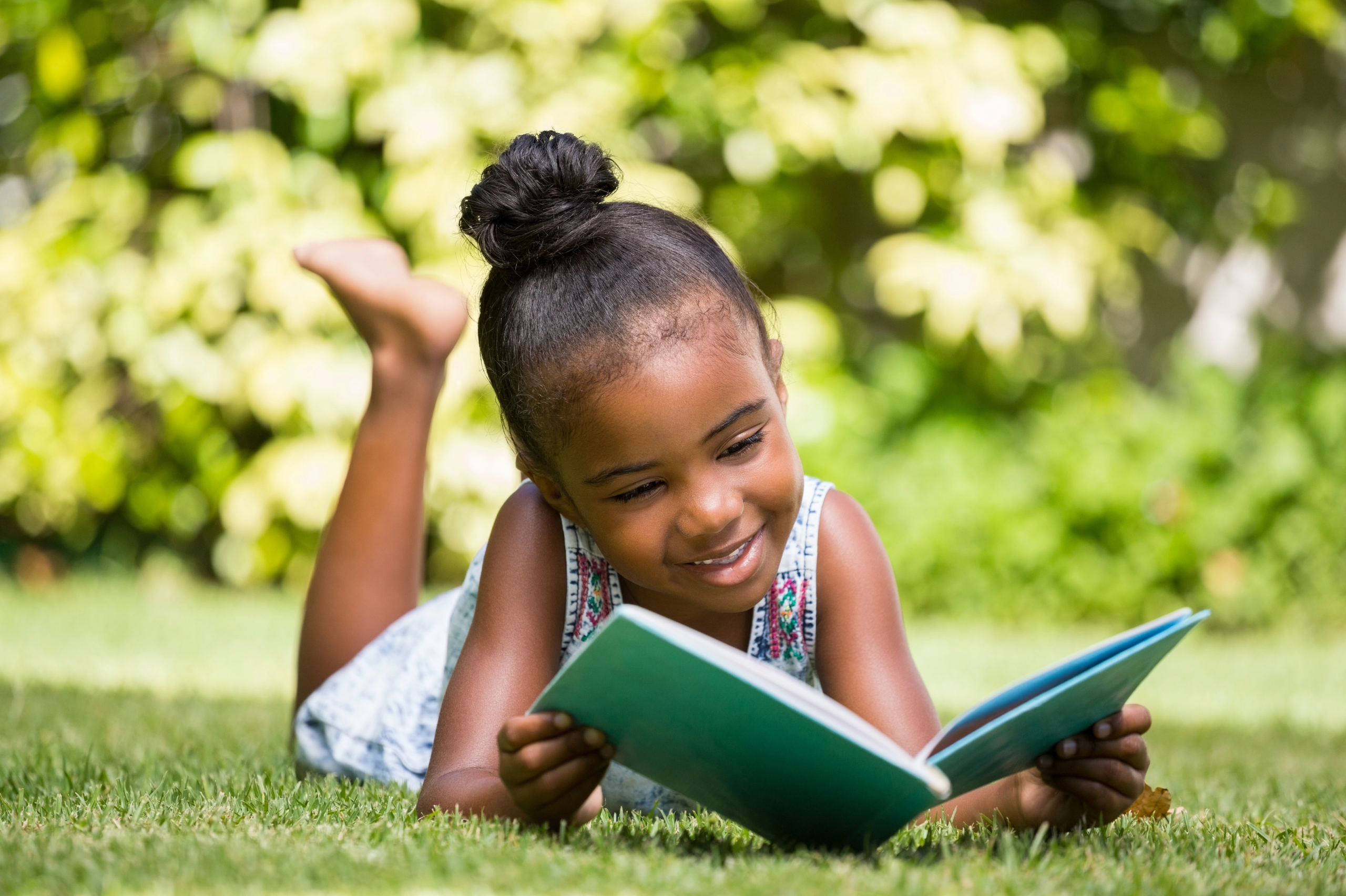 young black girl laying in the grass outside reading in the summer